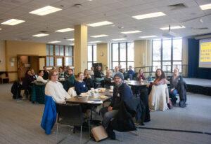 Photo of faculty during a faculty on campus work retreat. People are smiling and seated around tables.